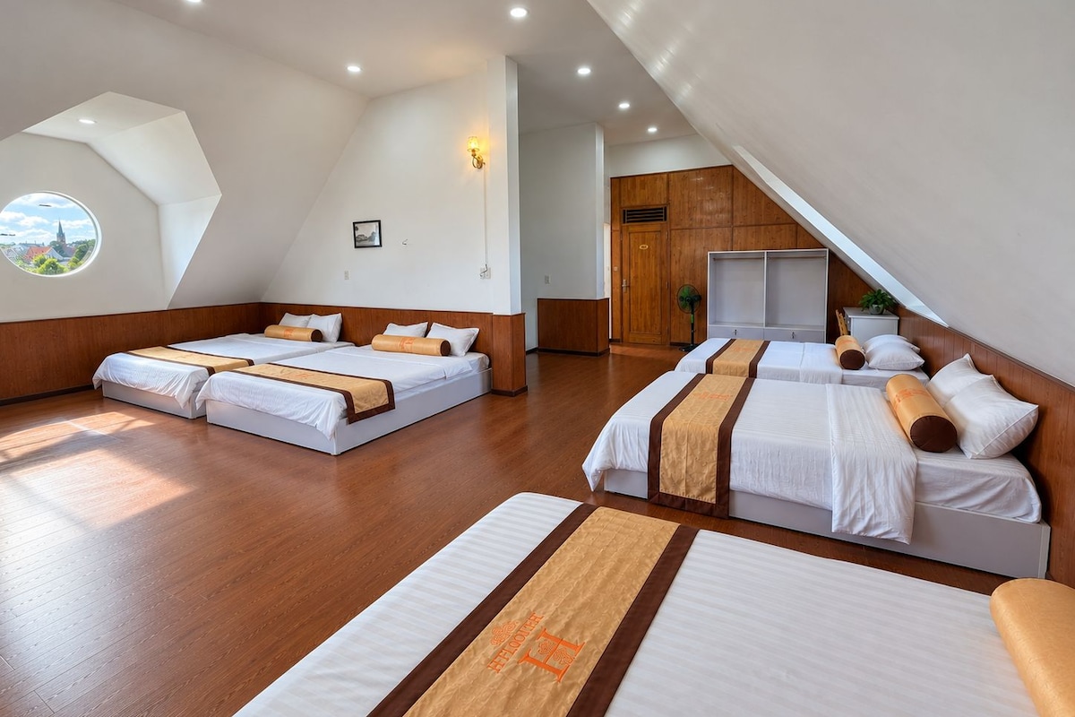Habitación de hotel con techo inclinado, dos camas con cabeceros a juego, un ventanal redondo con vistas y un armario de madera.