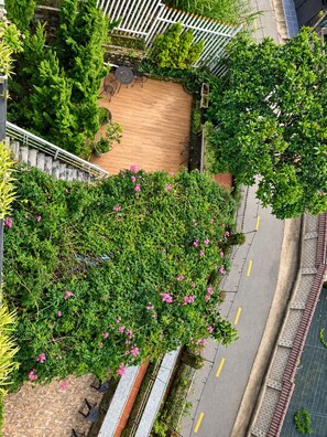 Un jardín en la azotea con terraza de madera, rodeado de abundante follaje y flores rosadas.