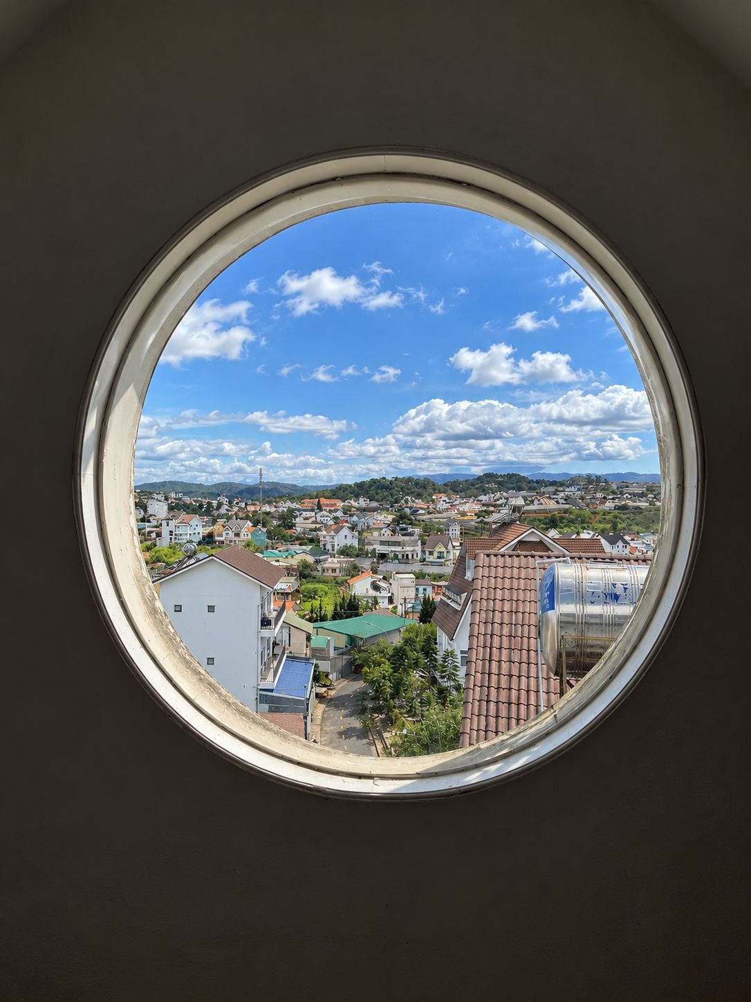 Finestra rodona amb vista a una vila, edificis i una serralada de muntanyes.