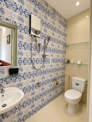 Casa de banho com sanita branca, lavatório e chuveiro com prateleira de vidro acima.