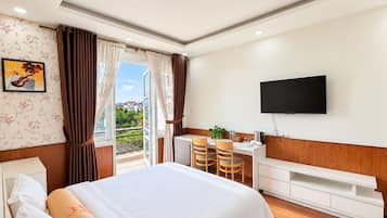 Une chambre d’hôtel comprenant un lit, un bureau avec des chaises, une télévision et un balcon avec des rideaux.