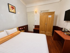 Quarto de hotel com cama, guarda-roupa de madeira, secretária com chaleira e televisão.