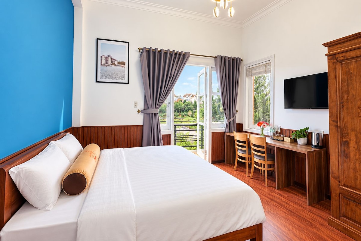 Habitación de hotel con cama, escritorio con sillas, televisor y vistas al exterior.