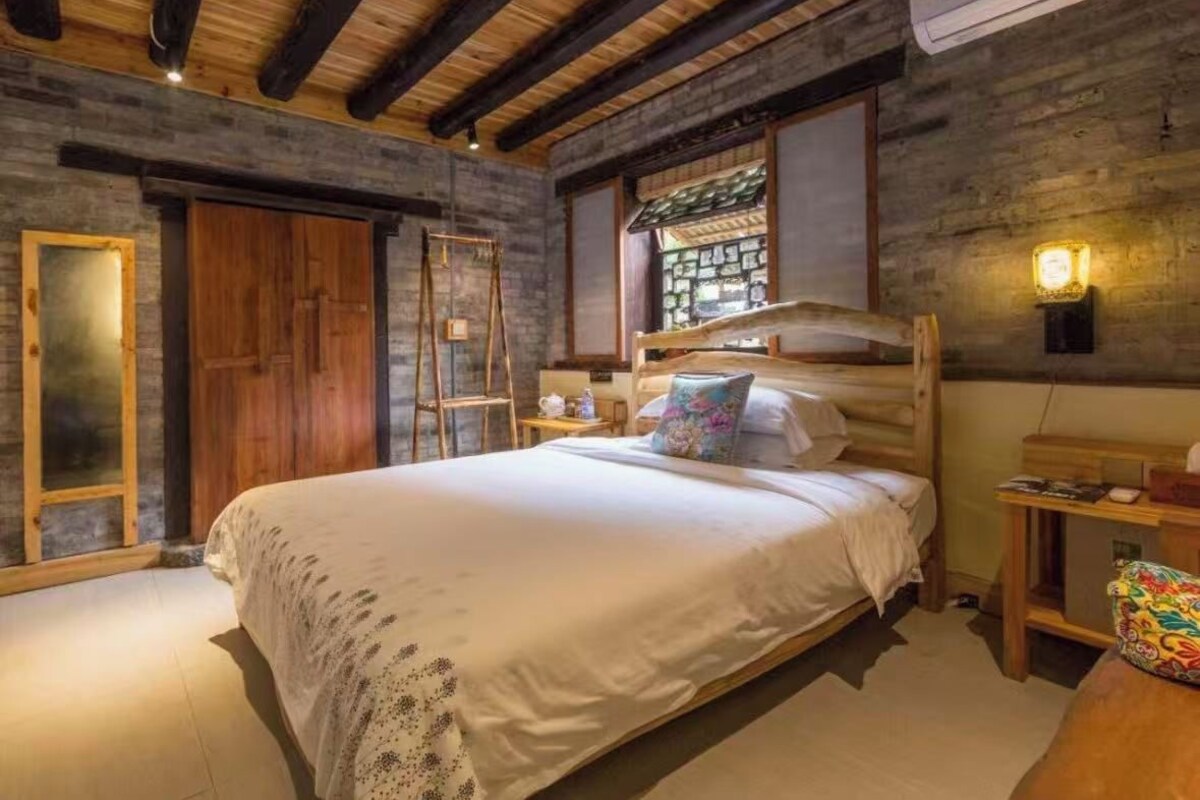 Une chambre à coucher avec un lit en bois, une armoire en bois, une fenêtre donnant sur un beau paysage et un luminaire fixé au mur.