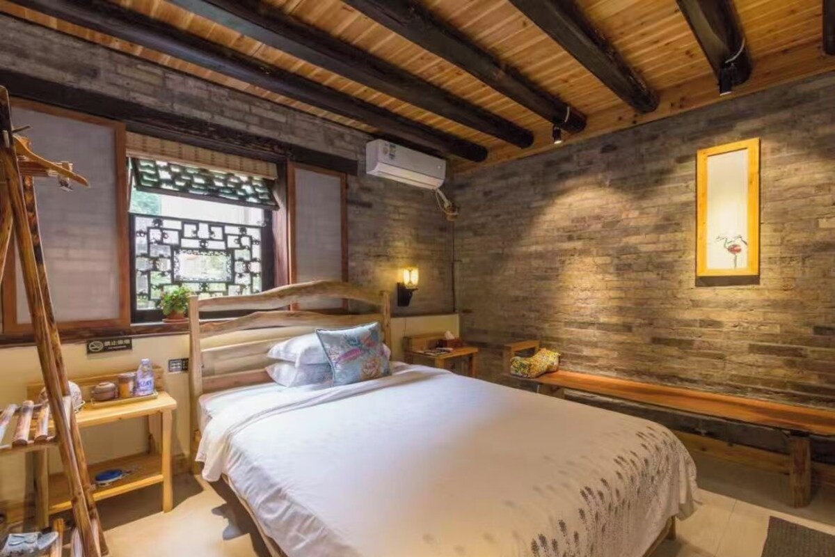 Une pièce avec un lit superposé, un banc en bois, une petite table avec une lampe et un climatiseur fixé au mur.