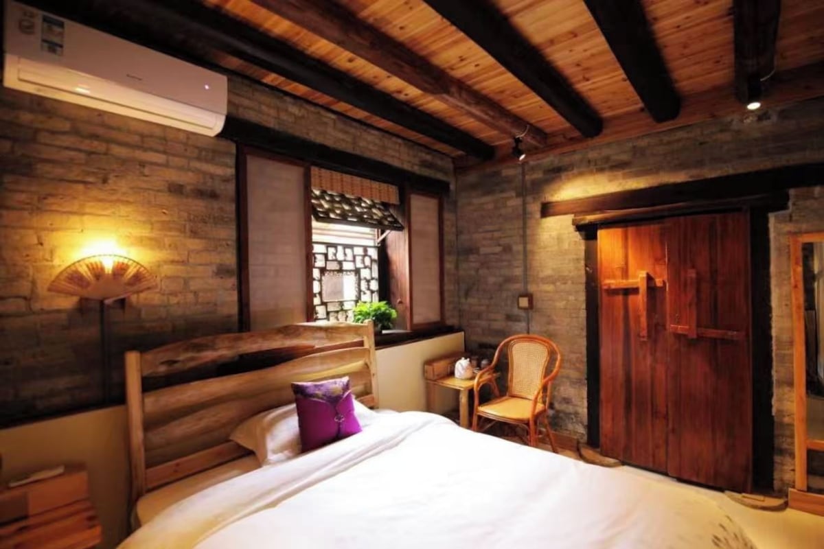 Une chambre à coucher avec un lit en bois, une chaise, une fenêtre donnant sur un beau paysage et une armoire en bois.