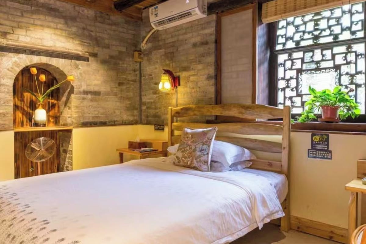 Une chambre à coucher avec un lit en bois, une table de chevet, une lampe et une fenêtre donnant sur un paysage verdoyant.
