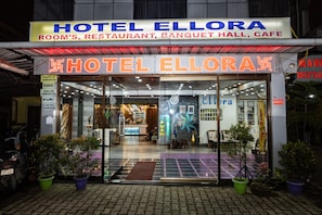 Exterior del Hotel Ellora con un letrero que indica que ofrece habitaciones, un restaurante, un salón de banquetes y una cafetería.