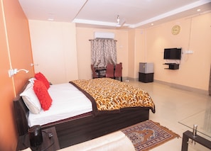 Una habitación de hotel con cama, escritorio, silla, televisor y refrigerador.