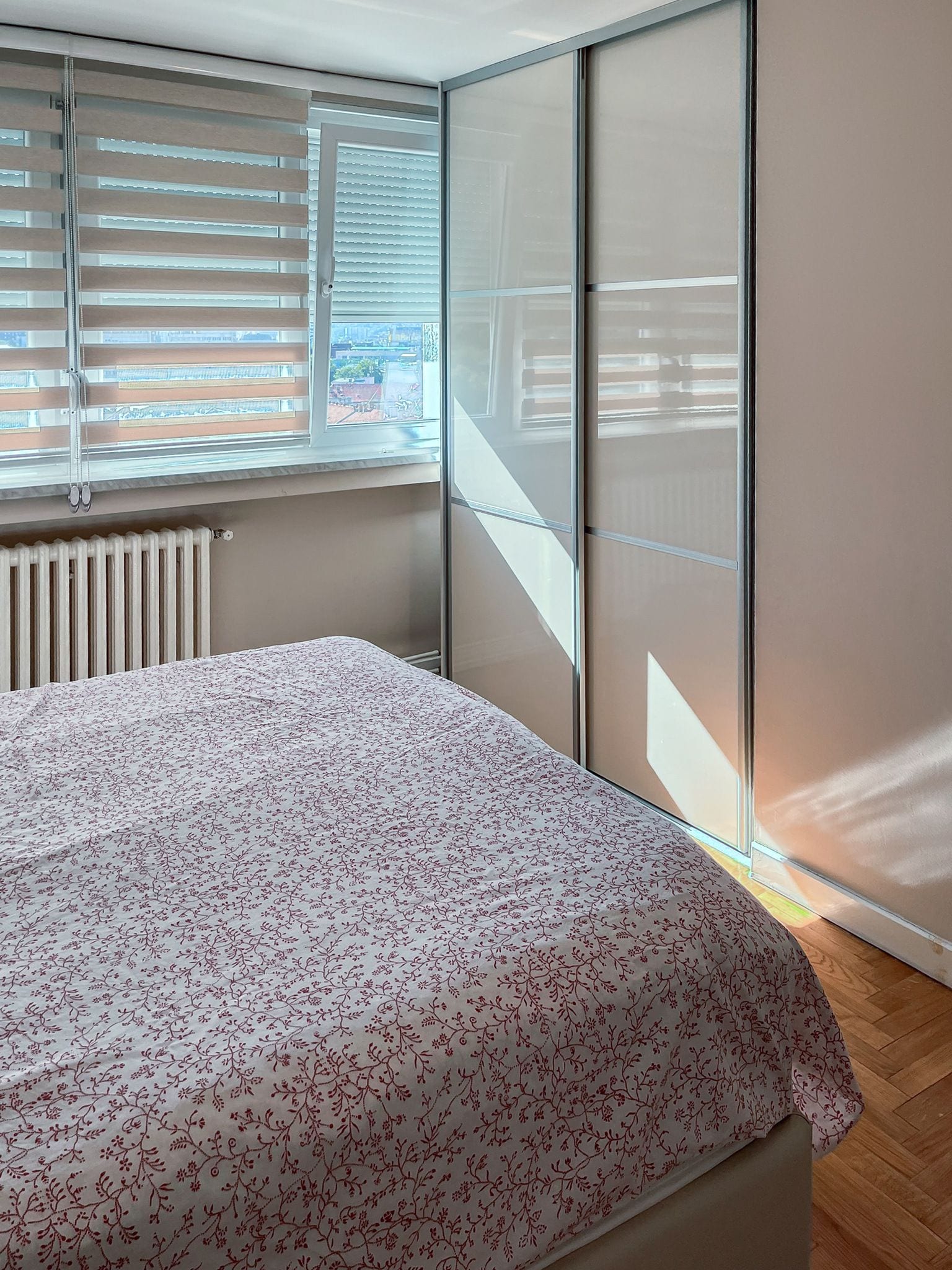 A bedroom with a bed, a radiator, and a window with blinds.