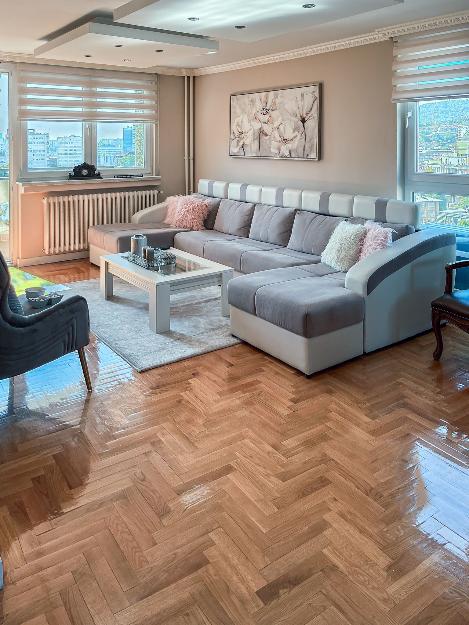 A modern living room with a large sectional sofa, a glass coffee table, and a herringbone hardwood floor.