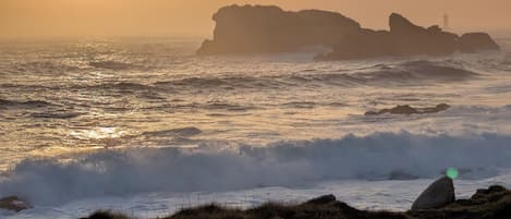 A coastal landscape with a rocky outcrop and waves at sunset.