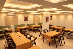 A dining area with multiple tables and booths, air conditioning units, and artwork on the walls. - Hotel Legacy Heights (Padinjare Vemballur)