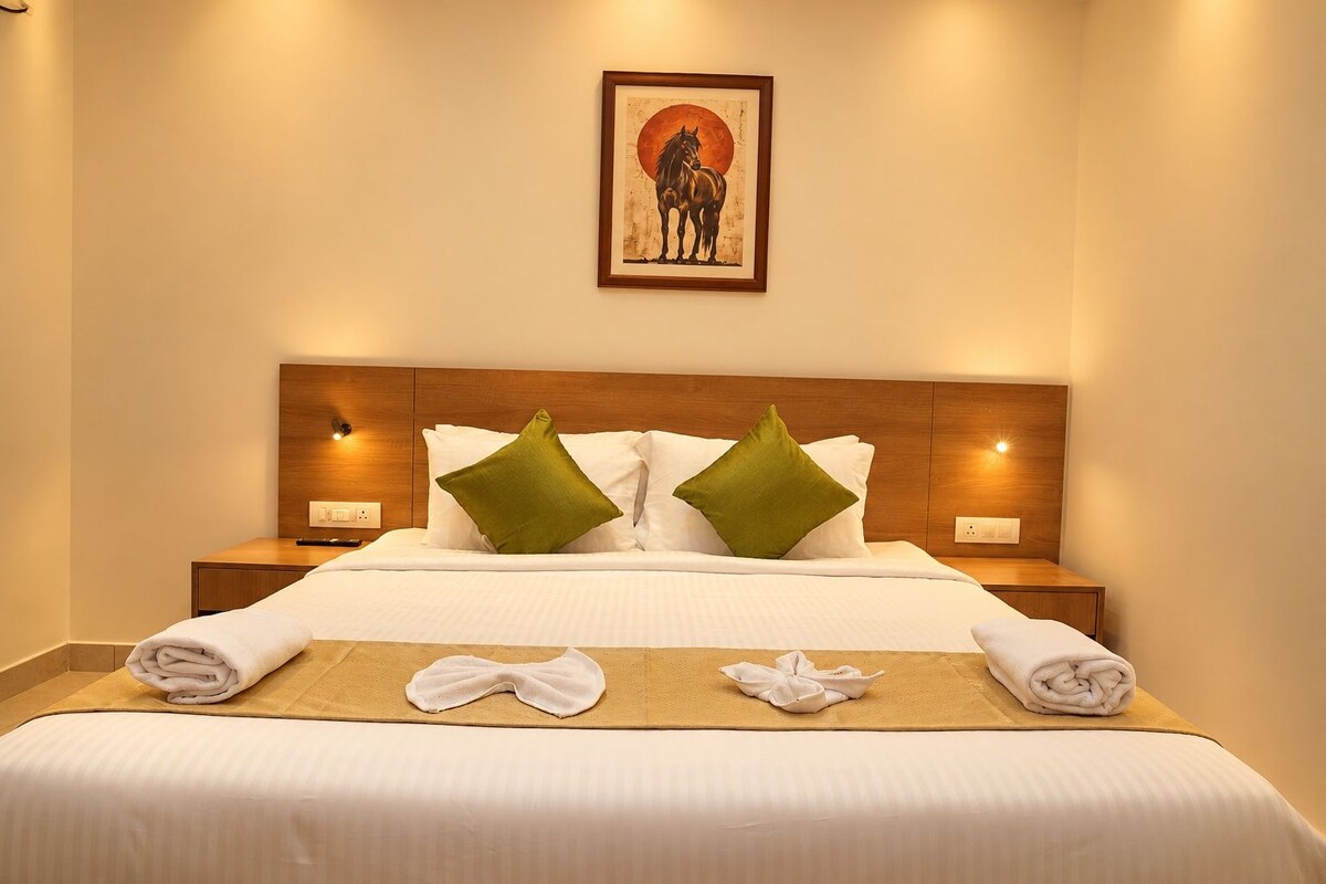A neatly made bed with white linens, two green pillows, and a framed artwork above it.