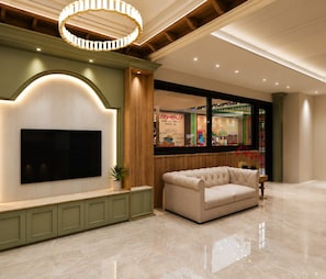 A modern living room with a flat-screen TV, a tufted sofa, and a wooden accent wall. - Aryan Inn Hotel (Varanasi)