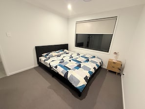 A bedroom with a bed, a window, a nightstand, and a wall-mounted lamp. - Spacious Private Bedrooms in Shared House (Morayfield)