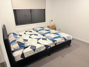 A bed with a geometric patterned bedspread, a bedside table with a lamp, and a window above the bed. - Spacious Private Bedrooms in Shared House (Morayfield)