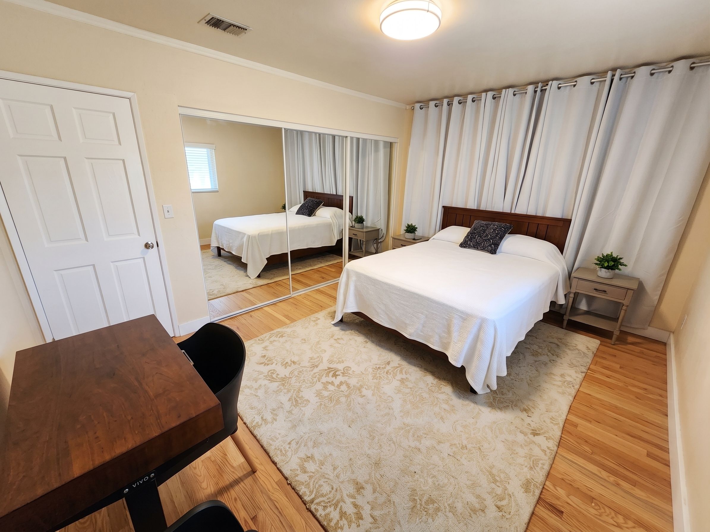 A bedroom with a large bed, a desk, and a mirror.