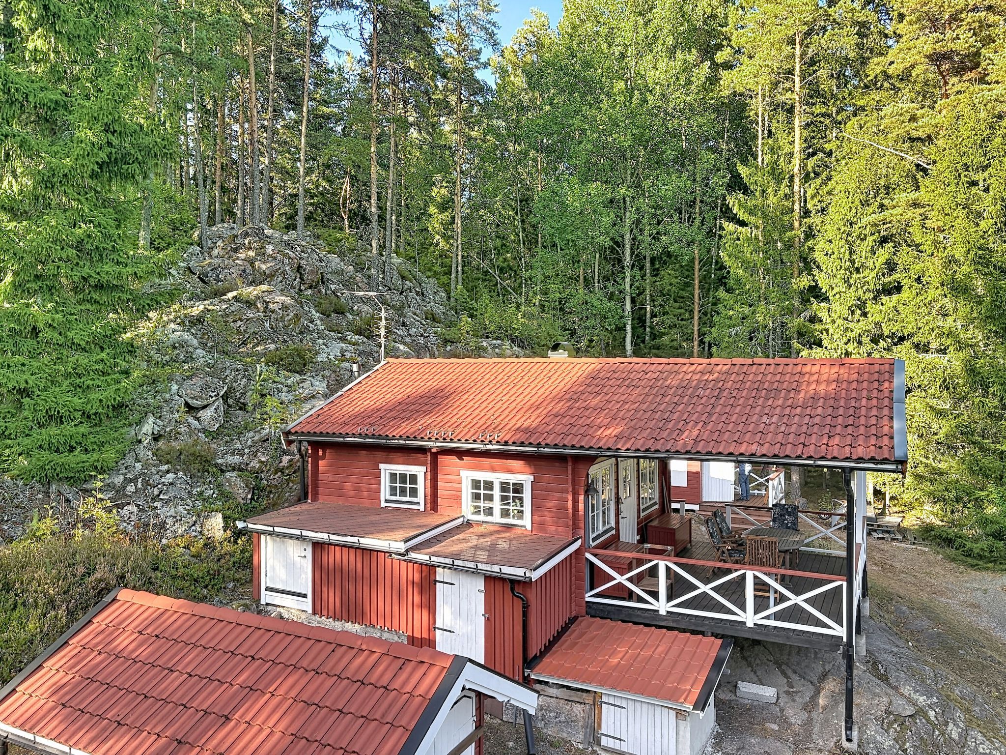Punakatolla varustettu puinen mökki, jossa on kuisti ja josta avautuu näkymä metsäiselle alueelle.