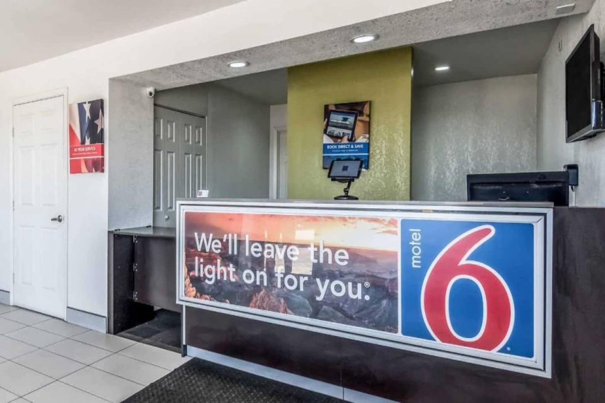A motel reception desk with a sign that reads 'We'll leave the light on for you.'