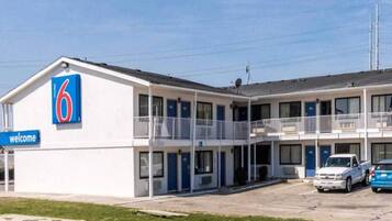 A motel with a '6' sign, a 'welcome' sign, and a parking lot with two cars.