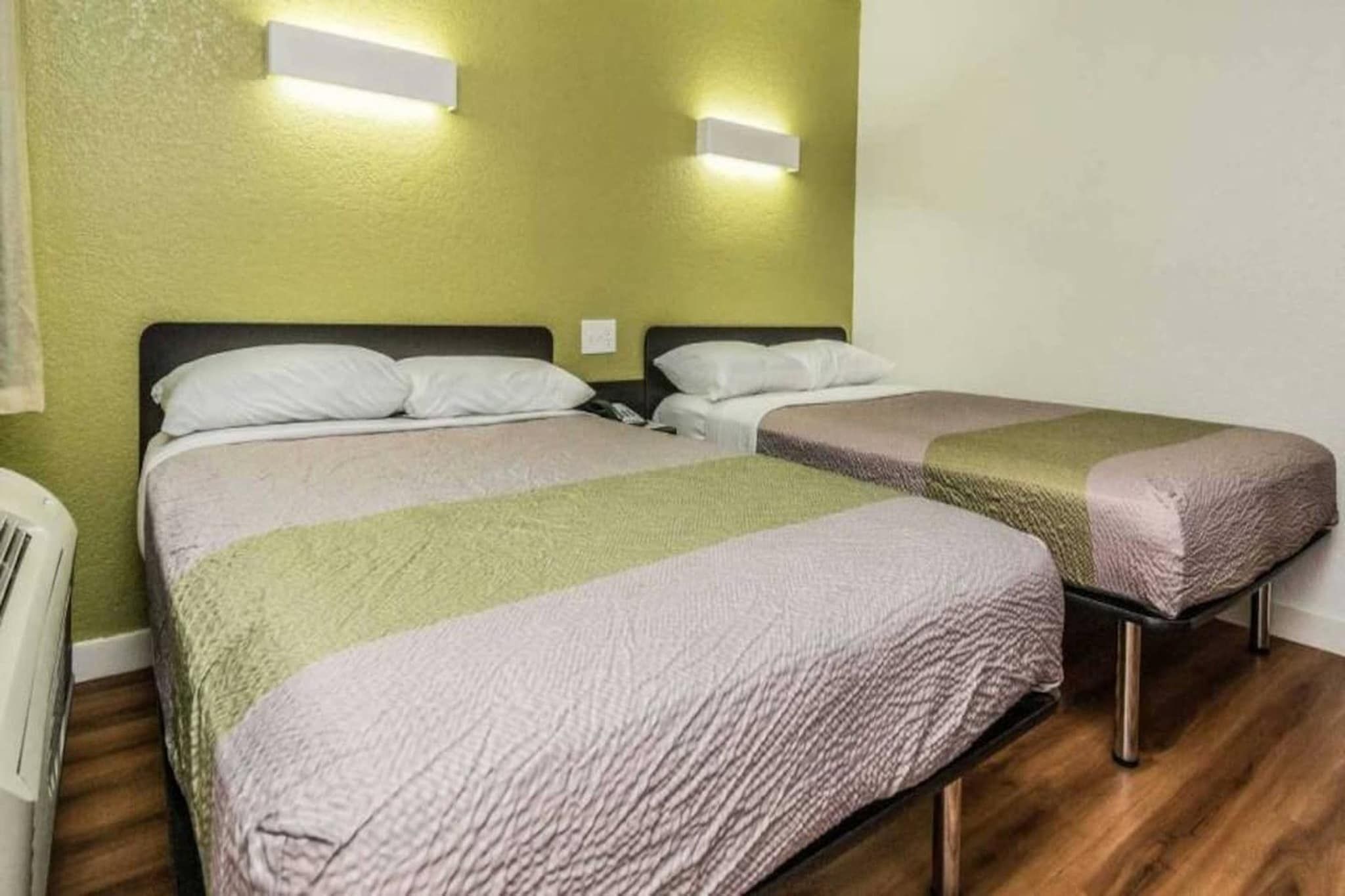 A room with two beds, each with a pillow and a blanket. There are wall-mounted lights above the beds.
