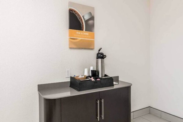 A kitchenette area with a coffee maker, a black tray with utensils, and a poster on the wall. - 1 Queen Bed | Non-Smoking (Fort Worth)