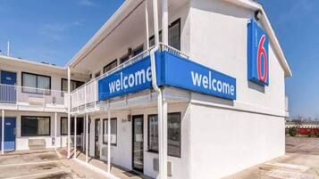 A motel with a 'Welcome' sign, a covered parking area, and a clear sky.