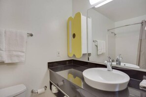 A modern bathroom with a white sink, a large mirror, and a towel rack. - 1 Queen Bed | ADA/Tub, Non-Smoking (Stafford)