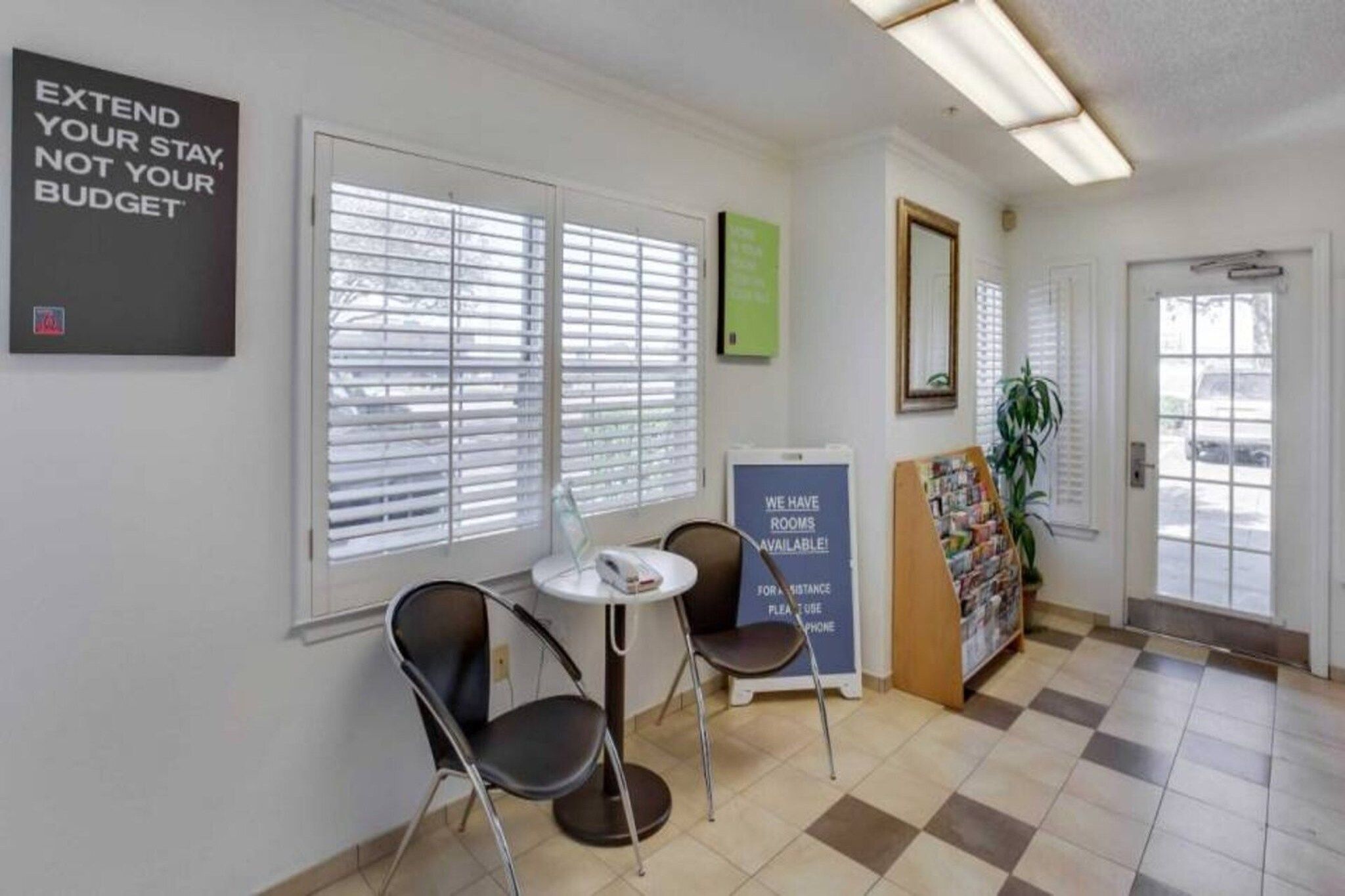 Zona de recepción con mostrador de entrada, dos sillones, un tablón de anuncios y una puerta que da al exterior.