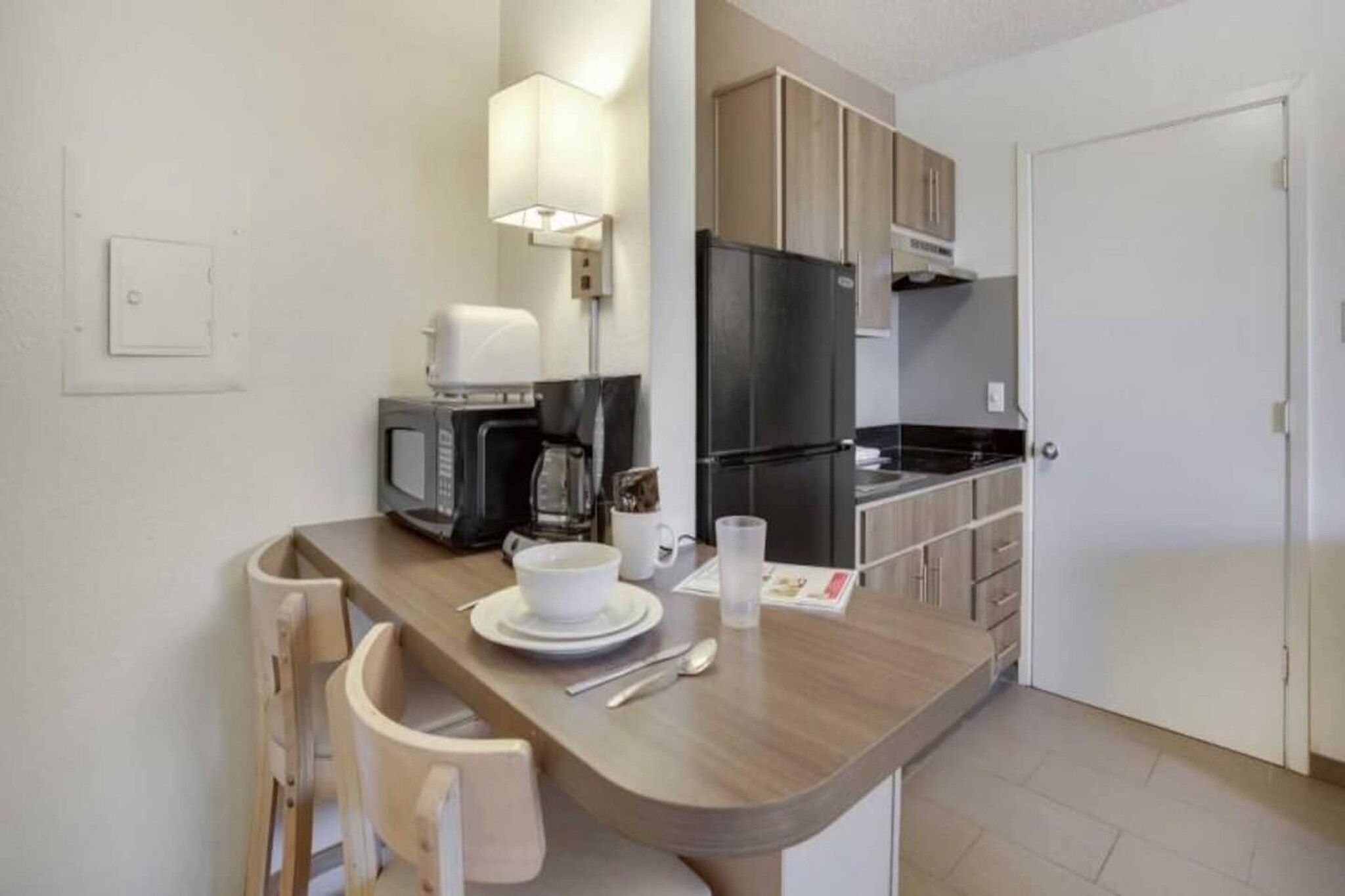 Una kitchenette compacta equipada con microondas, cafetera y un pequeño comedor con una silla y una mesa.