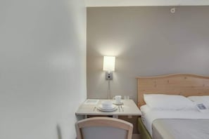 Una habitació d'hotel amb un llit, una tauleta de nit amb una làmpada i una cadira.