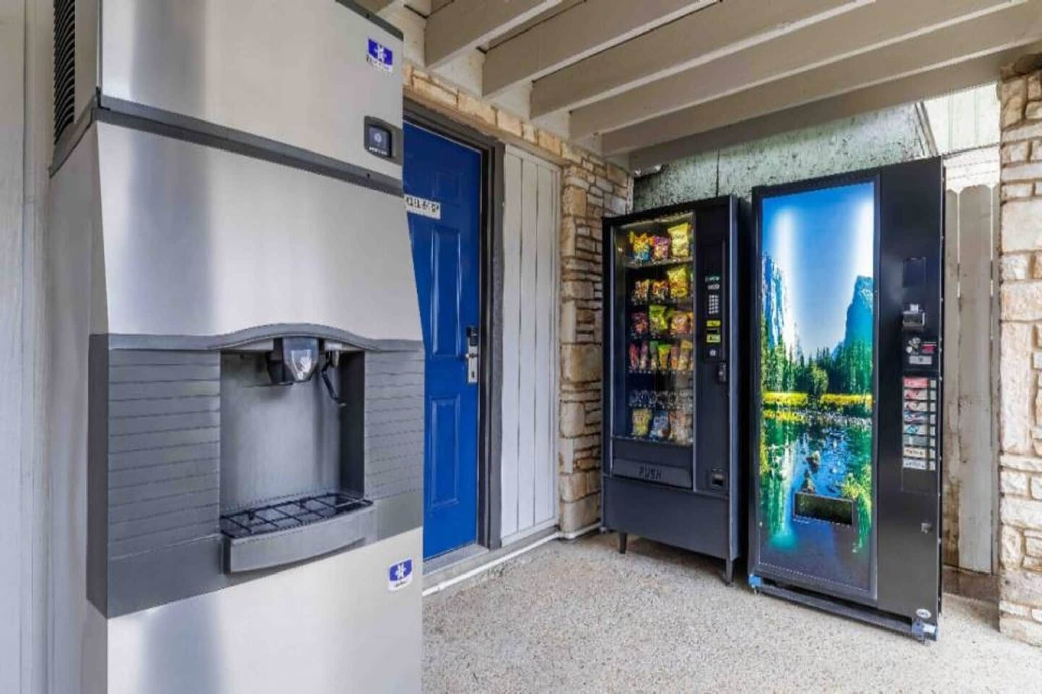 A water dispenser and two vending machines outside a building with a stone wall and a blue door.