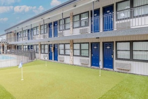 Um hotel com vários andares, piscina, quartos individuais com portas azuis e área externa cercada.
