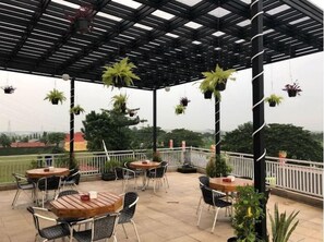 Un patio al aire libre con mesas y sillas, plantas colgantes y vistas del paisaje.