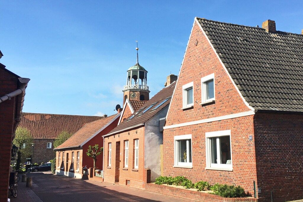 A street with traditional brick buildings, a church with a bell tower, and a clear blue sky.