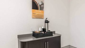 A kitchenette area with a coffee maker, a black tray with utensils, and a poster on the wall.