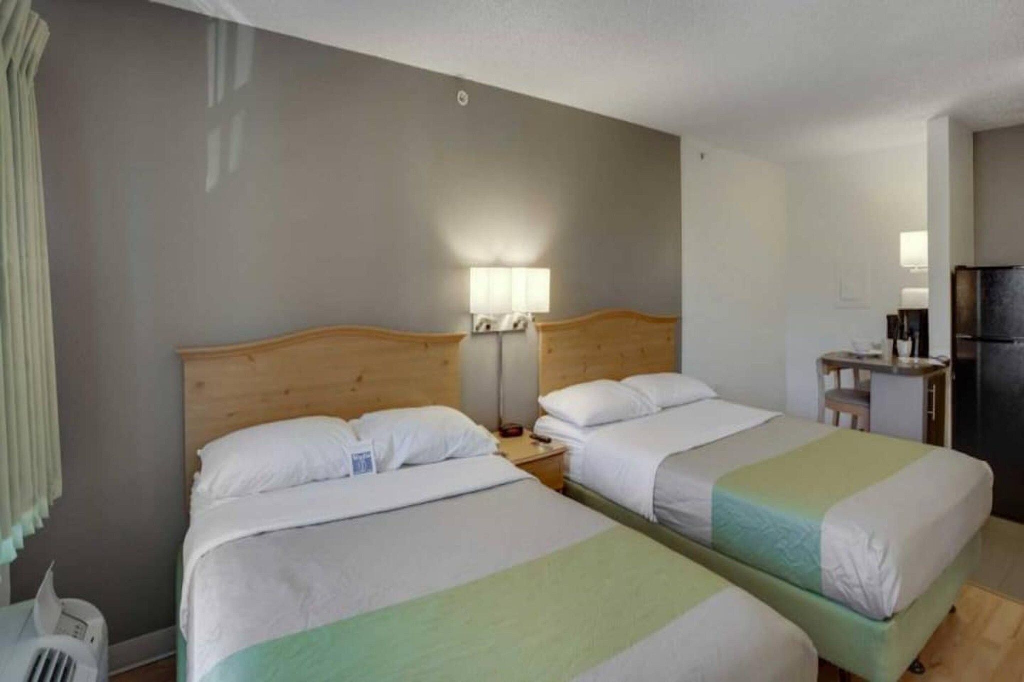 Una habitación de hotel con dos camas, un escritorio pequeño, un refrigerador y una mesita de noche con lámparas.