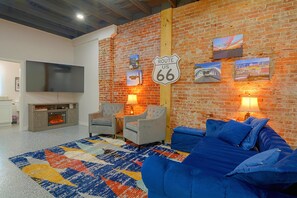 A living room with a brick wall, a Route 66 sign, a flat-screen TV, a fireplace, and a blue sofa. - Galena Route 66 Retreat w/ Historic Brick Style (Galena)