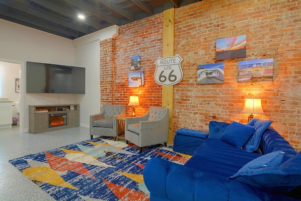 Una sala de estar con pared de ladrillo, un cartel de Route 66, un televisor de pantalla plana, chimenea y sofá azul.