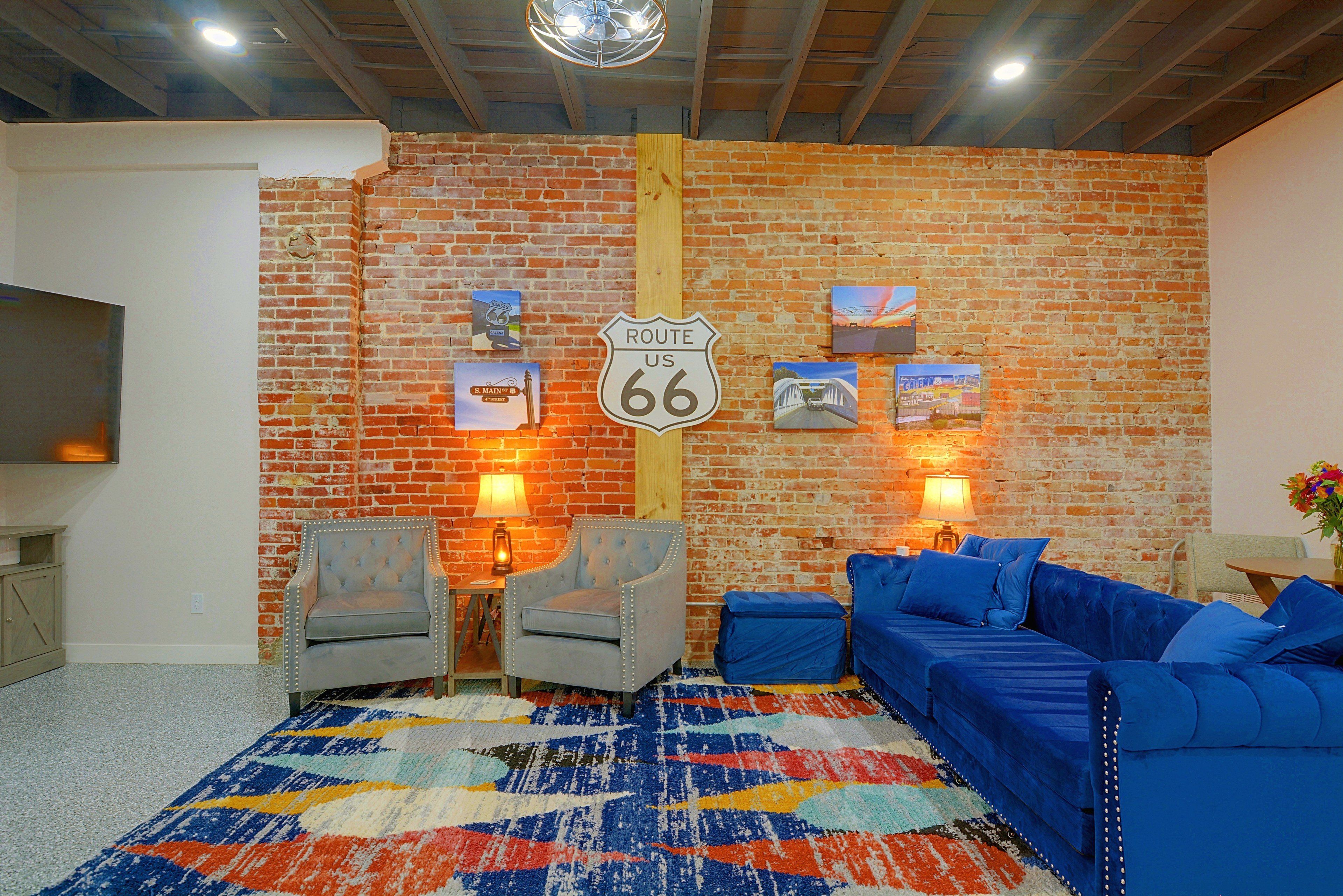 Ein Zimmer mit einer Ziegelwand, einem Route 66 Schild, zwei Sesseln, einem blauen Sofa und einem farbenfrohen Teppich.