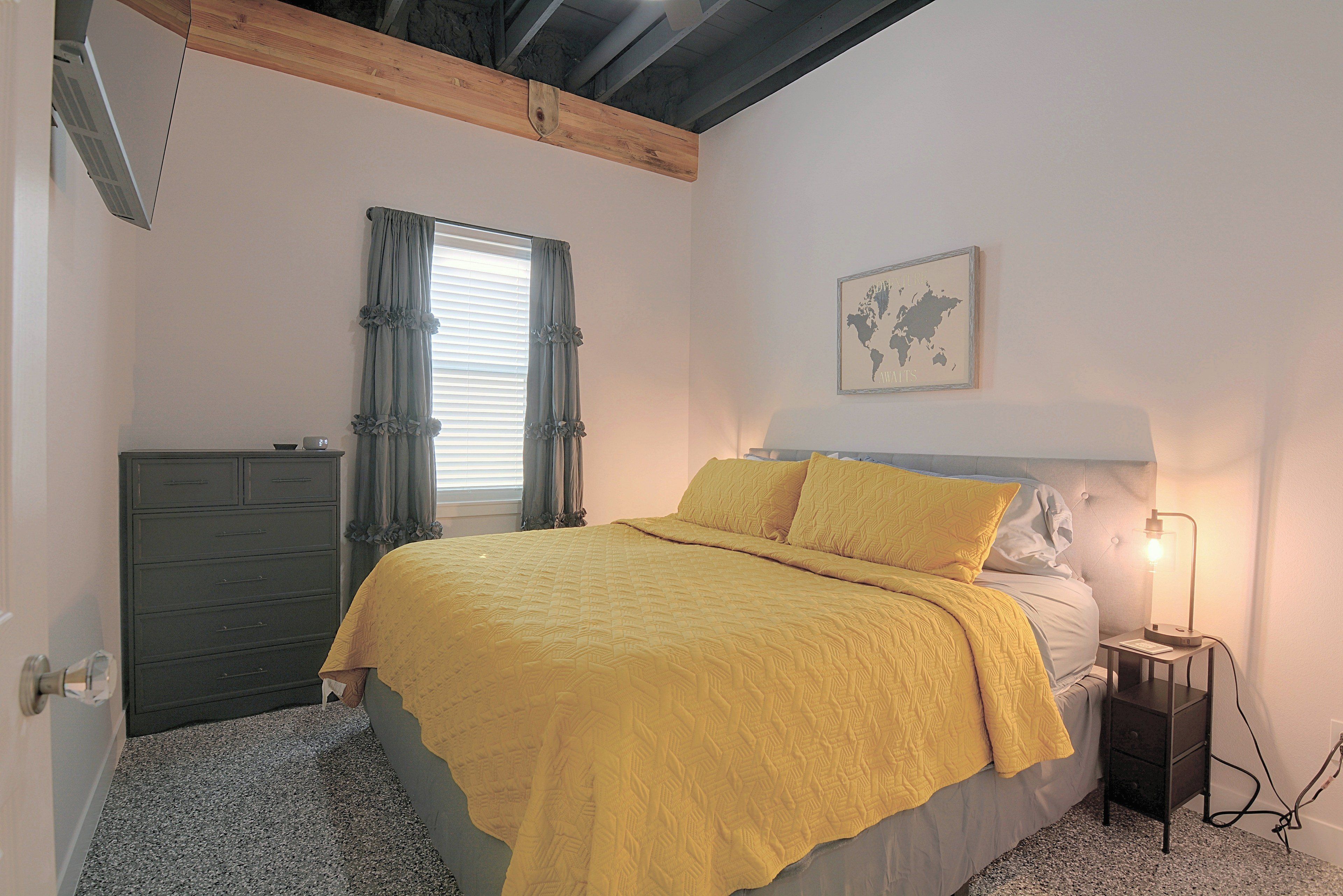 Un dormitorio con cama, mesita de noche, cómoda, ventana con cortinas y un mapa en la pared.