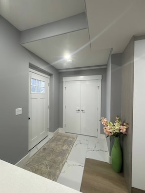 A hallway with a white door, a white wall, and a green vase with flowers.