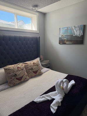 A bedroom with a large bed, a window, a painting, and a nightstand.