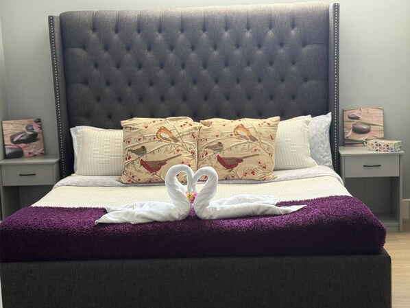 Ein Bett mit einer gebügelten Kopfteile, zwei dekorative Kissen mit Vogelmotiven und zwei Handtücher, die zu einem Herz geformt sind, auf einer violetten Decke.