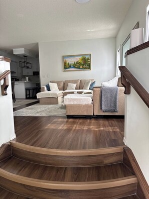 Ein Wohnzimmer mit einer Sofagarnitur, einem Bild an der Wand und einer Treppe, die in einen anderen Bereich führt.