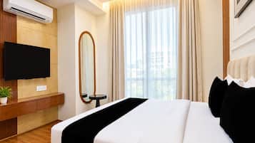 A hotel room with a bed, a flat-screen TV, a mirror, and a window with curtains.