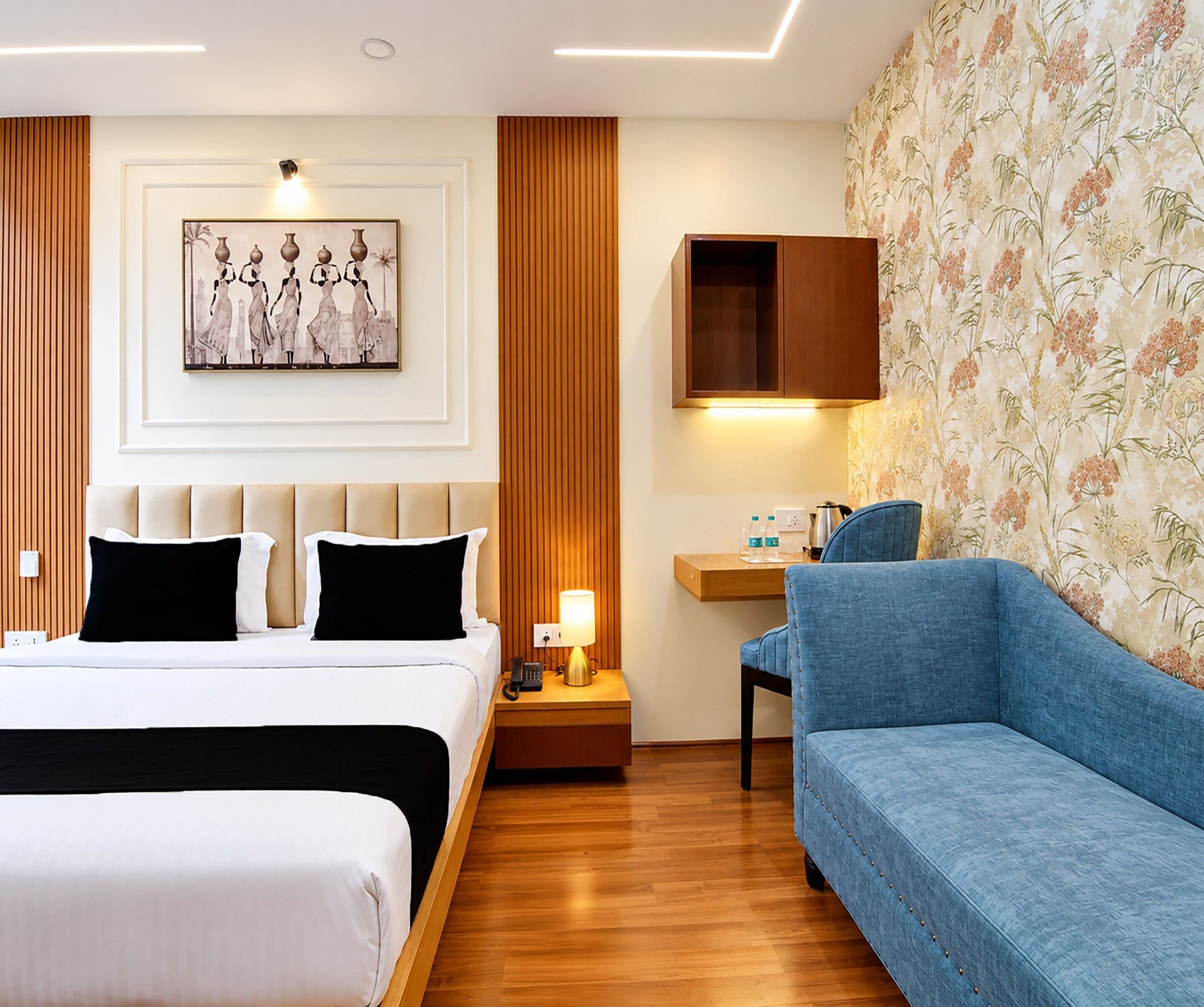 A hotel room with a bed, a sofa, a desk with a lamp, a telephone, and a wall-mounted cabinet.
