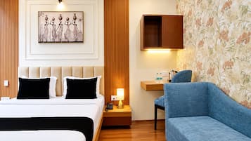 A hotel room with a bed, a sofa, a desk with a lamp, a telephone, and a wall-mounted cabinet.