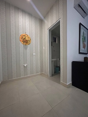 Una habitación con papel tapiz estampado, una puerta que da al baño y un cuadro en la pared.